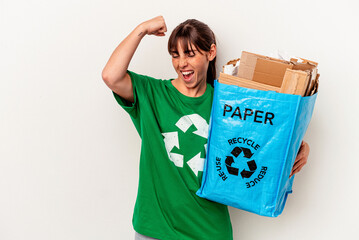 Young Argentinian woman recycled paper isolated on yellow background raising fist after a victory, winner concept.