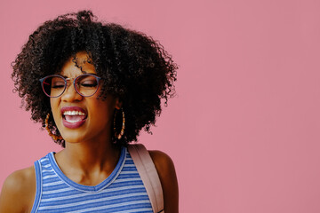 smiling young african american woman student in eyeglasses posing on pink background