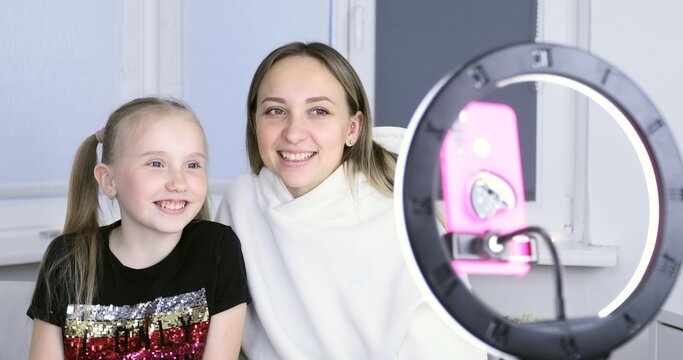 Mom and daughter are recording a video blog on a smartphone camera. A woman and a schoolgirl talk over video communication during quarantine.