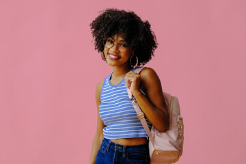 attractive girl in eyeglasses with backpack posing on pink background, back to school college...