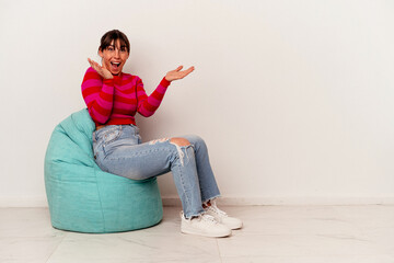 Young Argentinian woman sitting on a puff isolated on white background receiving a pleasant...