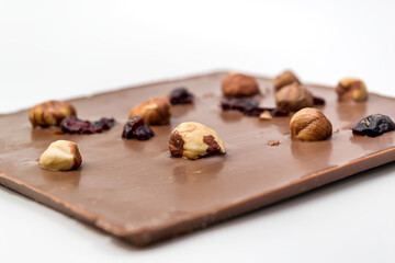 Hand crafted milk chocolate with hazelnuts, raisins and dried fruits on white background. Selective Focus