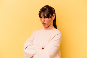 Young Argentinian woman isolated on yellow background frowning face in displeasure, keeps arms folded.