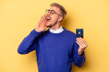 Young computer man isolated on yellow background shouting and holding palm near opened mouth.