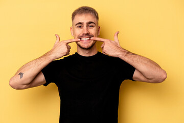 Young caucasian man isolated on yellow background smiles, pointing fingers at mouth.