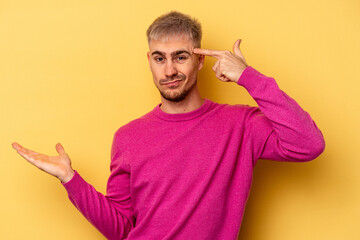 Young caucasian man isolated on yellow background holding and showing a product on hand.