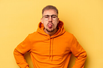 Young caucasian man isolated on yellow background funny and friendly sticking out tongue.