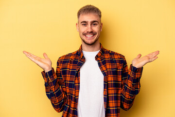 Young caucasian man isolated on yellow background makes scale with arms, feels happy and confident.