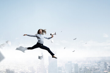 Fototapeta na wymiar Portrait of energetic businesswoman with megaphone jumping in open air