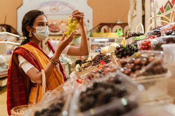 Young indian woman wearing face mask making purchases in eastern market