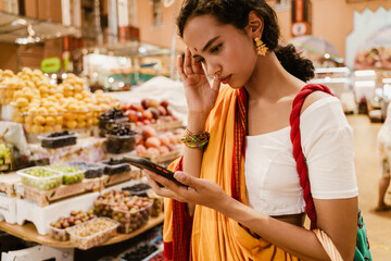 Young indian woman using mobile phone during shopping in eastern market