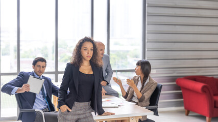 A young female manager in smart casual dress stands in arm crossed in front of other colleagues with confident to express ambitious target of their business strategy or plan. Young female executive