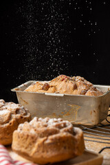 Close-up of unfocused plum cake, fresh out of the oven, with falling sugar, selective focus, black background, vertical