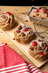 Top view of individual plum cakes, decorated with sugar, raisins and cherries, on wooden table with rustic red cloth, in vertical