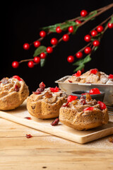 Close-up of individual plum cakes, decorated with sugar, raisins and cherries, selective focus, on rustic table, black background with red branches, vertical