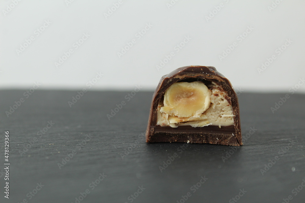 Wall mural chocolate candy with praline white filling and hazelnut hazelnut in section. Dessert candy lies on a black black background with space for copyspace text. Chocolate Day. Chocolate case candy