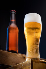 a glass of cold fresh light beer and a bottle of steamed cold beer in the background on a black background. a party or celebration in a beer restaurant