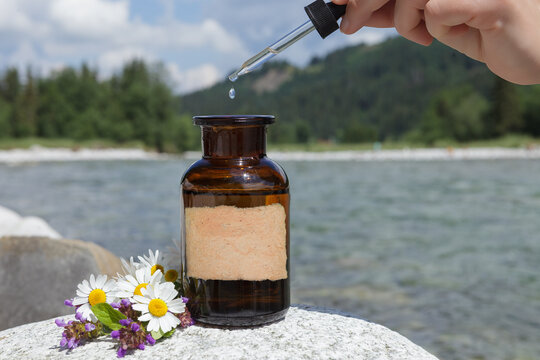 Conceptual image related to natural medicine. Drip from dropper falling into bottle. Old medical bottle against background of mountains. Empty label, mockup.