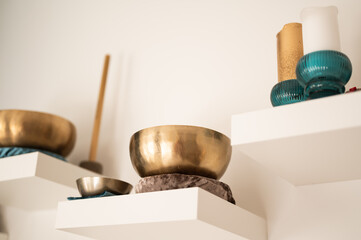 Tools for sound healing therapy - singing bowls and stick on white wall shelf. Alternative medicine concept.