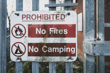 Shallow focus of a weathered, generic prohibited sign seen attached to a metal fence, leading to an...