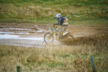 a motorcyclist riding his motorbike across a water-logged muddy track 