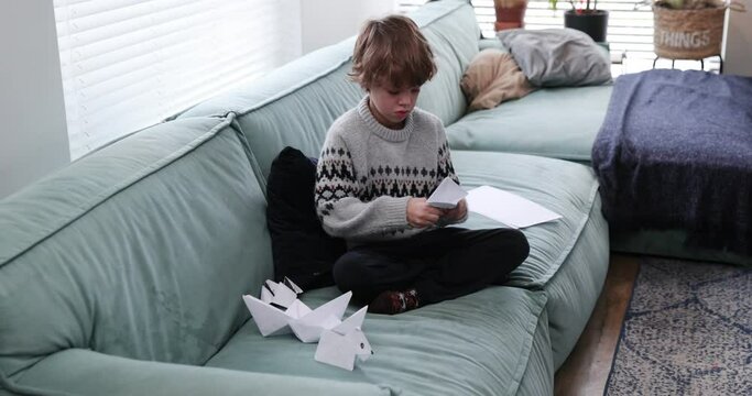 Boy makes paper ship . Boy sitting on the sofa folds origami, a paper boat