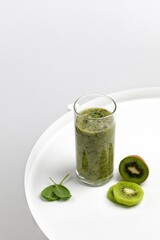 Green smoothie in a glass with slices of kiwi and spinach on white round table