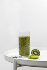 Green smoothie in a glass with slices of kiwi and spinach on white round table