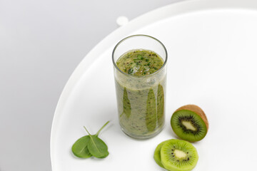Green smoothie in a glass with slices of kiwi and spinach on white round table