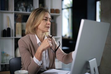 Attractive middle aged woman working at office, using contemporary desktop computer.