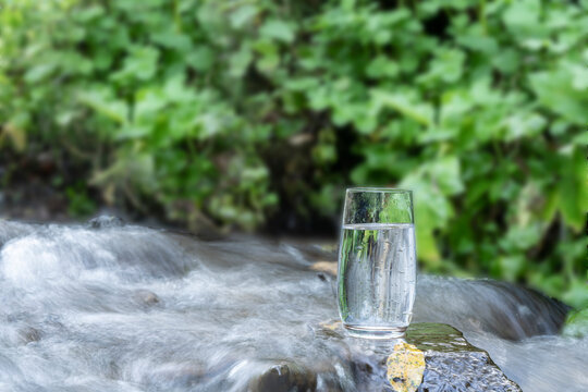 a glass of clean transparent drinking water in a transparent glass on a stone in a green forest near a stream or mountain spring. healthy food and diet, beautiful background © VLRS