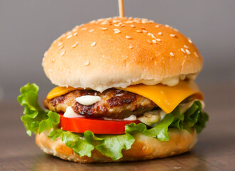 Fresh crispy chicken burger with cheese, tomatoes and lettuce on wood table, American fast food.