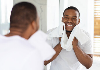 Male Beauty Care. Smiling African American Man Wiping Face With Towel In Bathroom