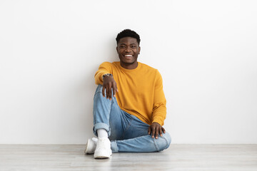 Positive afican american stylish guy sitting on floor by wall