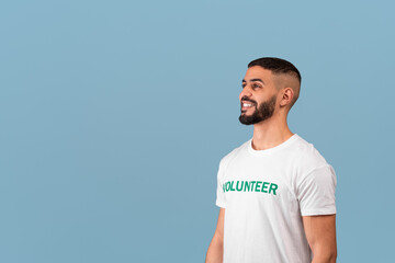 Young arab volunteer guy looking aside at free space for advertisement text and smiling, blue background, empty space