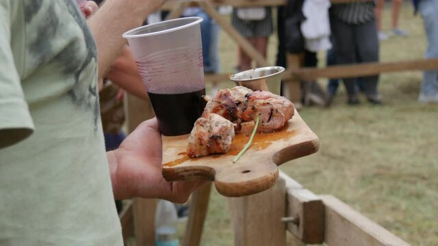 Juicy sliced pork knuckle is ready on a board next to wine in the hands of a man at a food festival