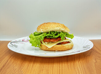 Fresh crispy chicken burger with cheese, tomatoes and lettuce on wood table, American fast food.