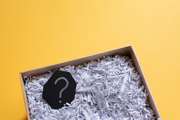 Question mark and shredded paper in abox against yellow background. Concept of Questions, recycle and secret