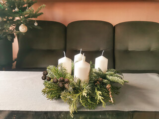 Christmas advent wreath with spruce and fir branches, tree cones and four white candles on the table.
