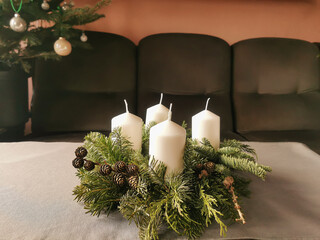 Handmade advent wreath with fir branches, tree cones and four white candles on the table. Christmas home decor.