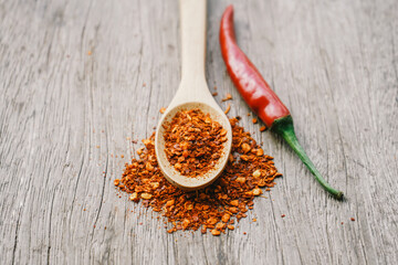 ground dried chillies in wooden spoon with fresh red chilli on wood background