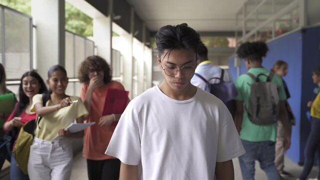 Sad Asian Teenager Victim Of Bullying At The High School. Abused Bullied Student Is Hit By Boy While Group Of Classmates Make Fun Of Him. Violence And Racism Problem In Education