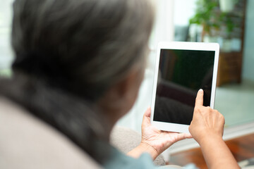 Senior asian woman wearing glasses and relaxing at home on a sofa and using tablet for reading news and e-book. Concept of technology for elderly.