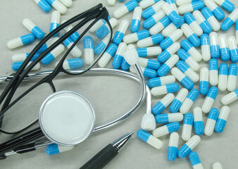 glasses, stethoscope, pens and blue and white pills scattered. medical concept