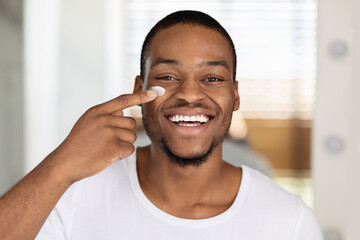 Closeup Shot Of Smiling Handsome Black Man Applying Moisturising Cream On Face