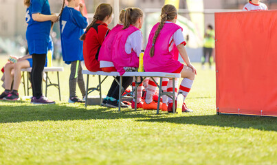 School girls sitting on football bench and watching tournament game. Female youth soccer team...
