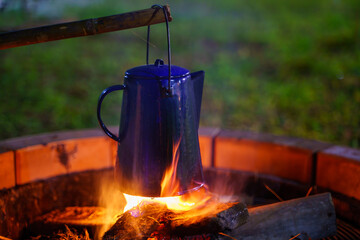 Selective focus vintage enamel kettle On the wood-burning stove in the night camping.antique coffee kettle. bonfire in the countryside.soft focus.shallow focus effect.