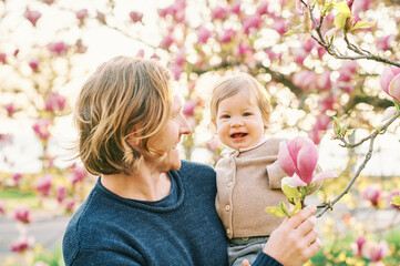 Outdoor portrait of happy young father playing with adorable toddler girl in spring park, looking...