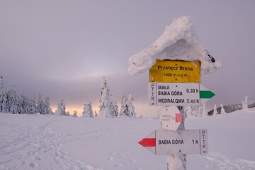Tourist signpost on Brona Mountain Pass. During winter trek to Babia Gora Mountain in winter scenery at sunrise light. Diablak, Beskid Zywiecki, Poland