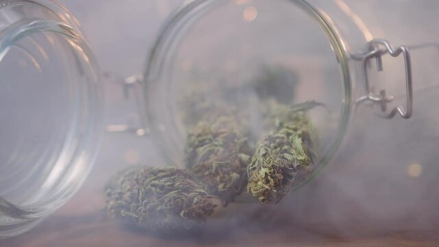 Close-up shot of a cannabis buds in a glass storage jar, in a cloud of smoke.